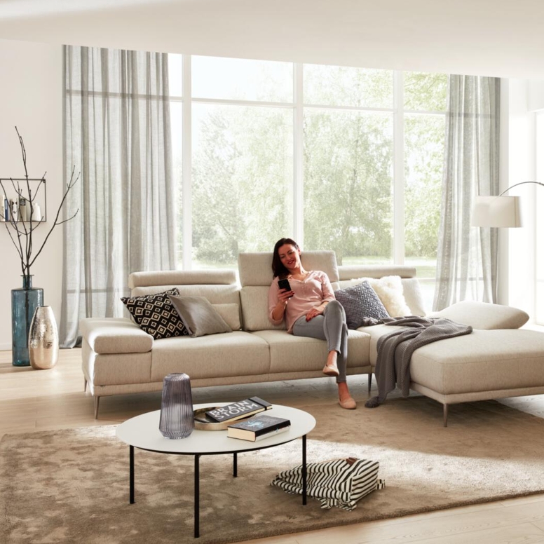 Frau entspannt ih ihrem Wohnzimmer auf modernem hellen Sofa.